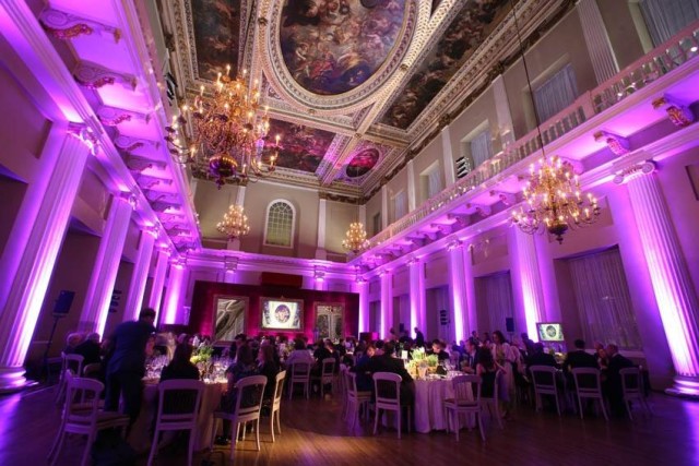 Main Hall with view of the grand painted ceilings with purple uplighters surrounding the room of round dining tables Banqueting House Venue Hire S