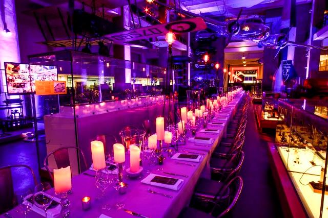 Exploring Space with long banqueting tables set for dinner with white linen and lit candles all the way down the table Science Museum Venue Hire, SW7