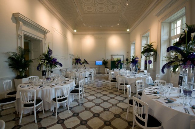Adam Hall set up for a dinner with natural daylight and round tables dressed in white linen with floral table decor Compton Verney Venue Hire CV35