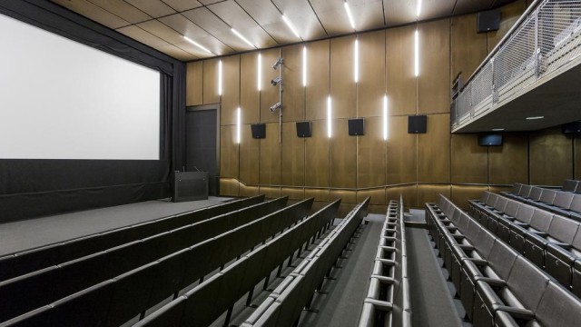 Lecture Theatre with tiered leather seating in theatre style with large screen and stage with modern wood paneling on the walls The Royal College of Art Venue Hire SW7