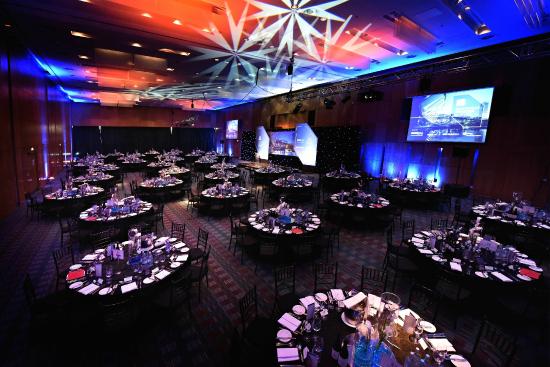 Deansgate Suite set for a large christmas party with high ceilings projecting light patterns, large screens on the walls and round tables set for dinner Hilton Manchester Deansgate Christmas Party M3